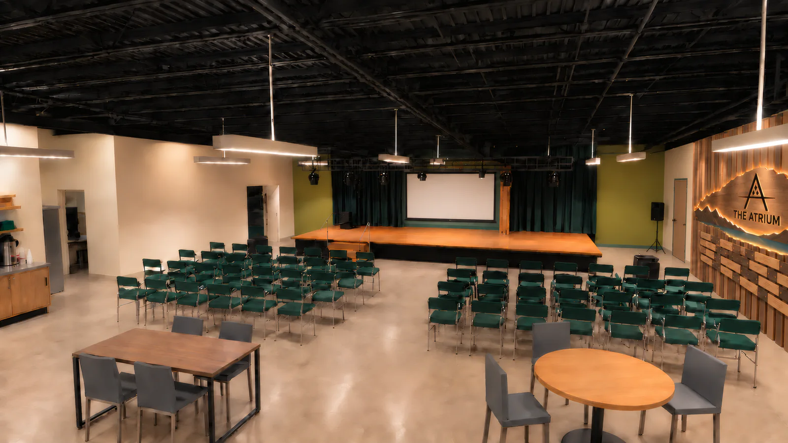 The event space: rows of green chairs facing a stage and screen, with a few tables at the back