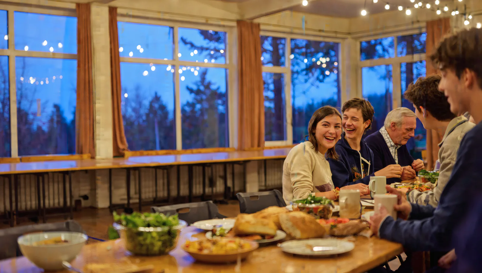 Students, parents and an older neighbour laughing together at a long table of shared food