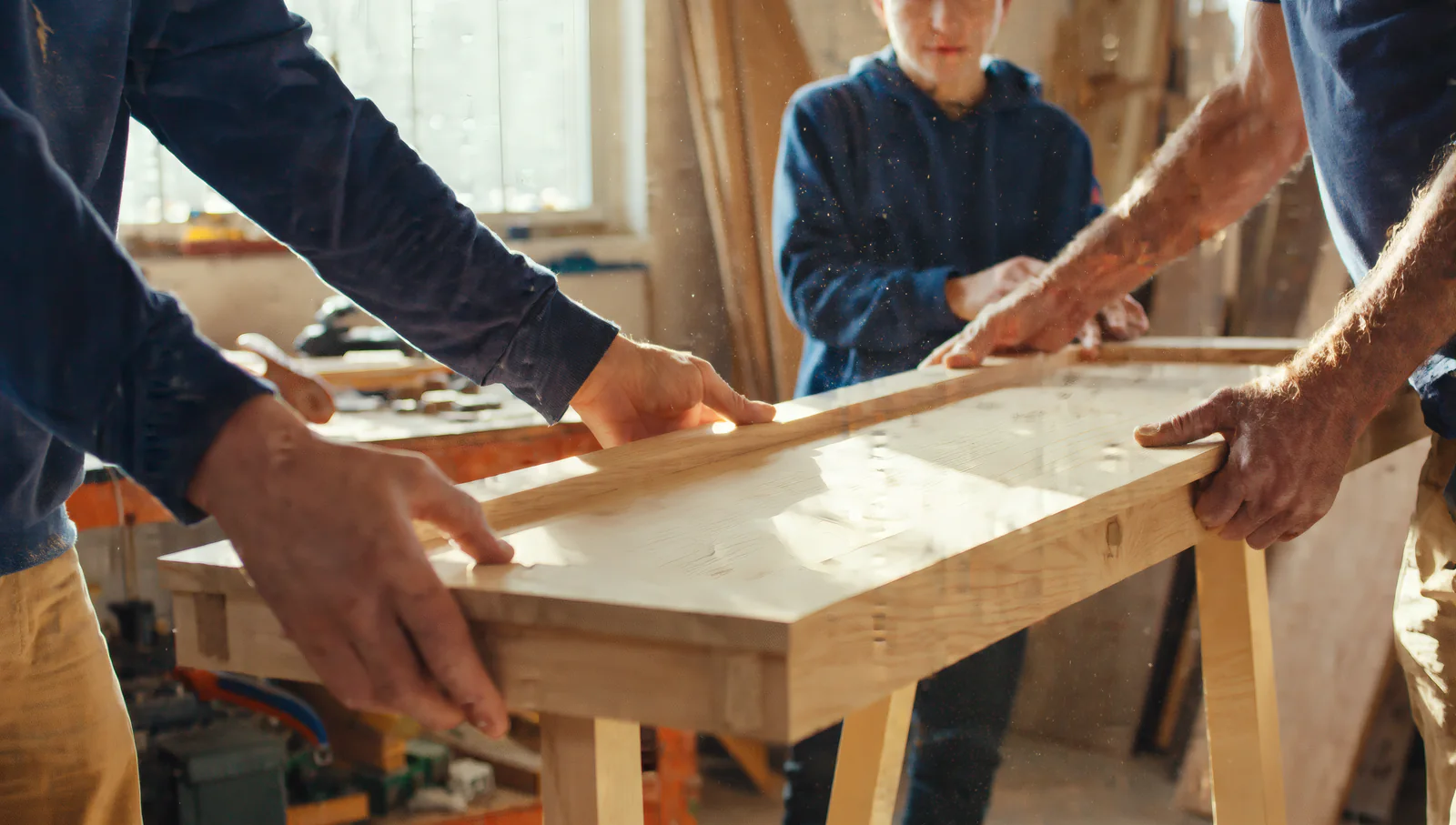 Three generations of hands lifting a freshly sanded workbench top together