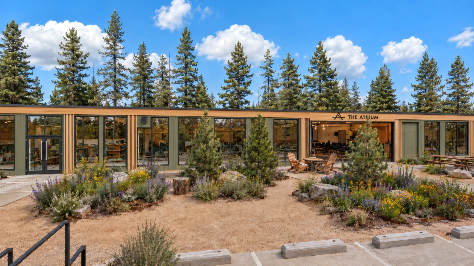 The courtyard in front of The Atrium: native plantings, boulders and stump seats, Adirondack chairs and picnic tables by the open roll-up doors, under tall pines